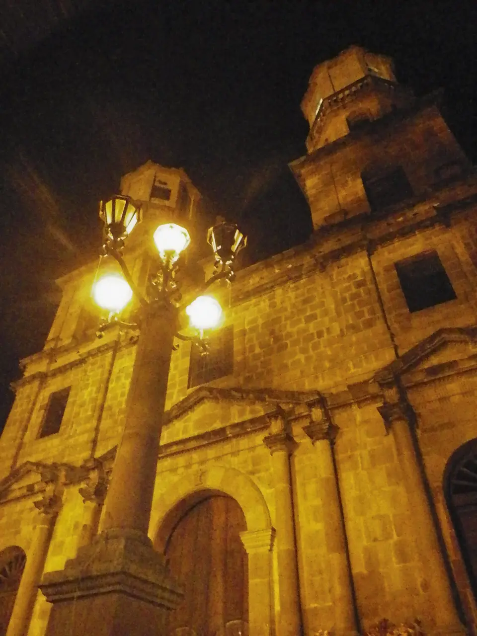 The Catedral de la Santa Cruz lit gold at night on San Gil’s main square, a street lamp in front.