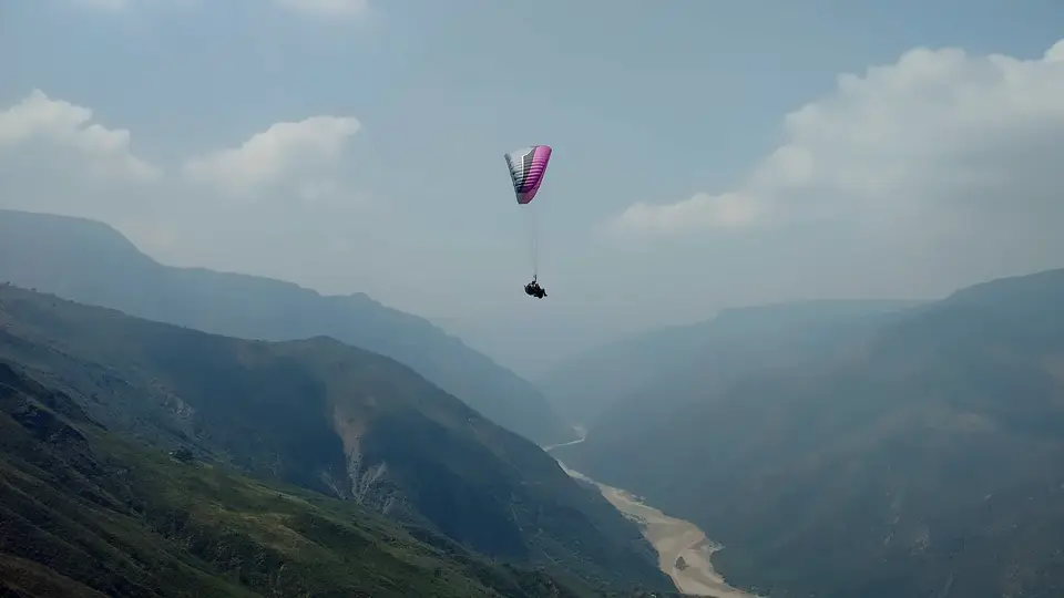 A paraglider high above the hazy Chicamocha Canyon, the river a pale line below.
