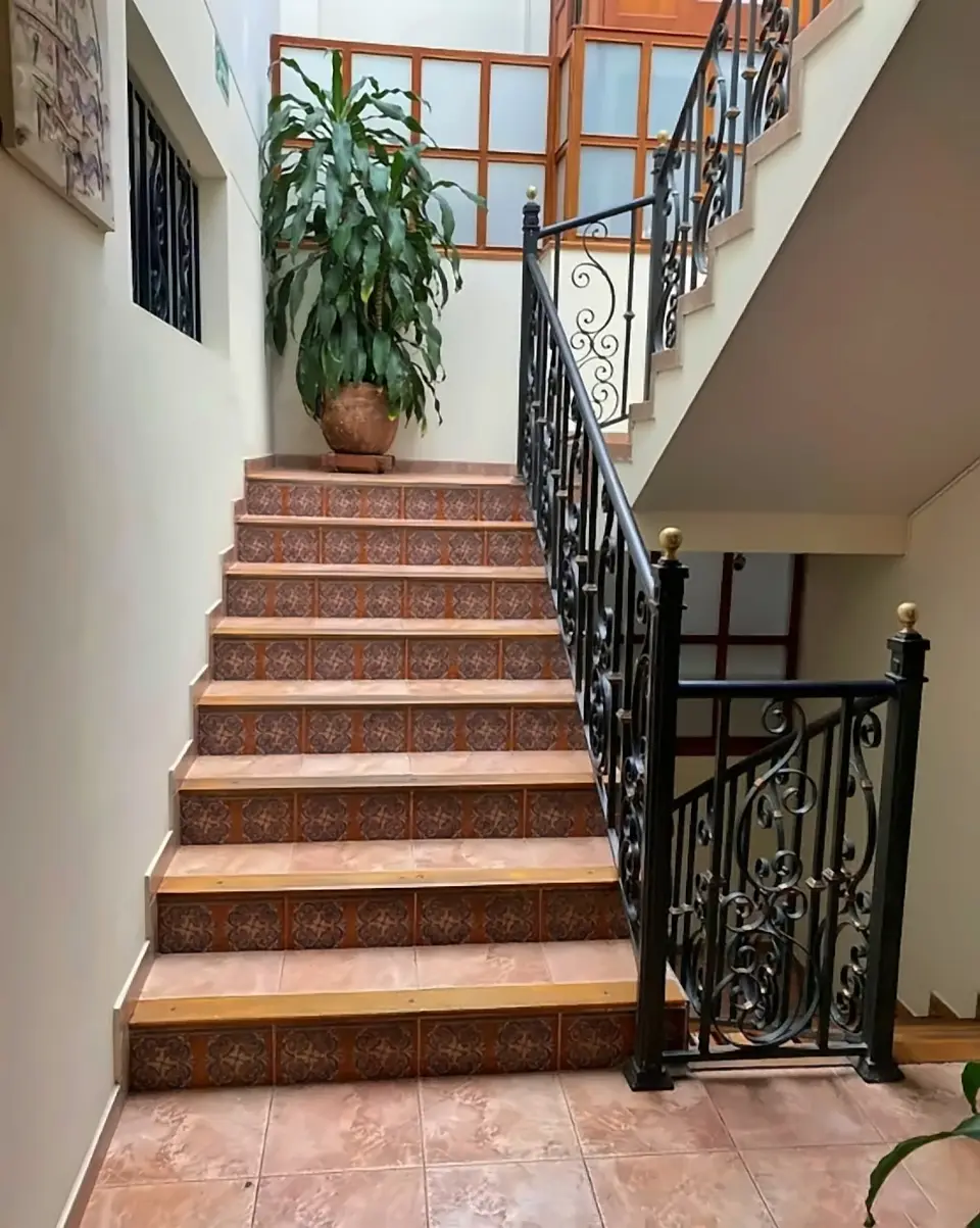 The interior staircase: terracotta-tiled steps, a wrought-iron banister full of scrolls and a big potted plant on the landing.